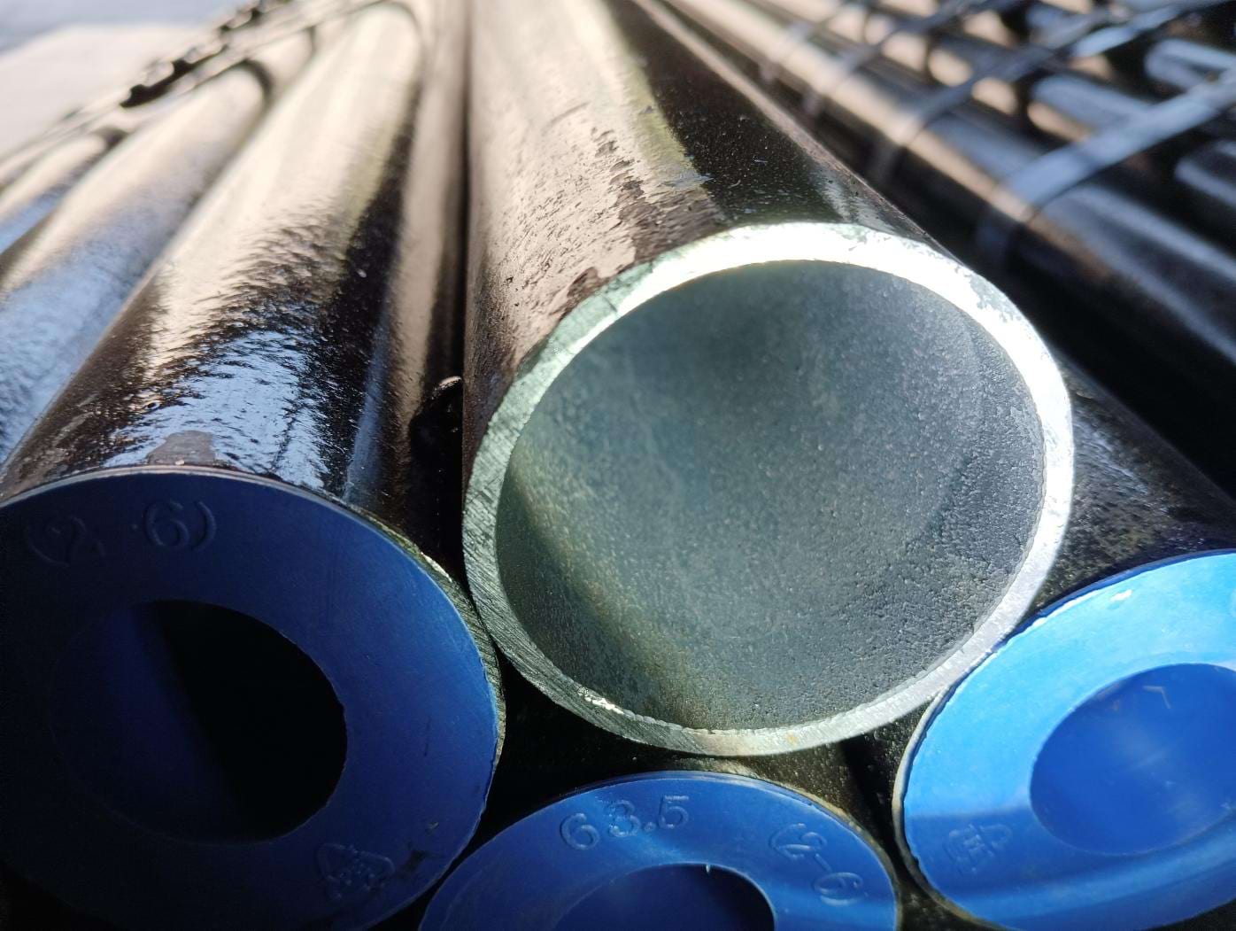 Extreme close-up of seamless tube ends showing the bare metallic bore of one tube alongside blue plastic end caps stamped with the tube size