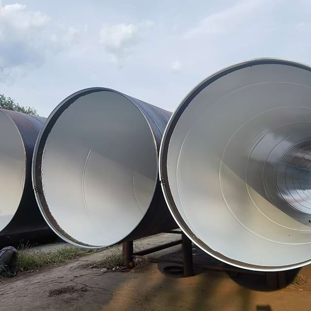 Three large-diameter coated pipes standing outdoors on supports with the lined interior bore visible