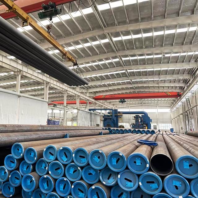 Seamless line pipe stacked with blue end caps under an overhead crane in a mill warehouse