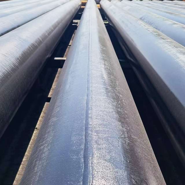 Coated welded LSAW line pipe on outdoor storage racks with the longitudinal weld seam visible along each length